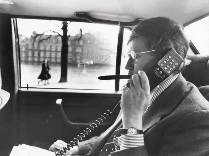 Minister Wiegel met een autotelefoon in de dienstauto; op de achtergrond het Binnenhof. Minister Hans Wiegel met een autotelefoon in de dienstauto; op de achtergrond het Binnenhof